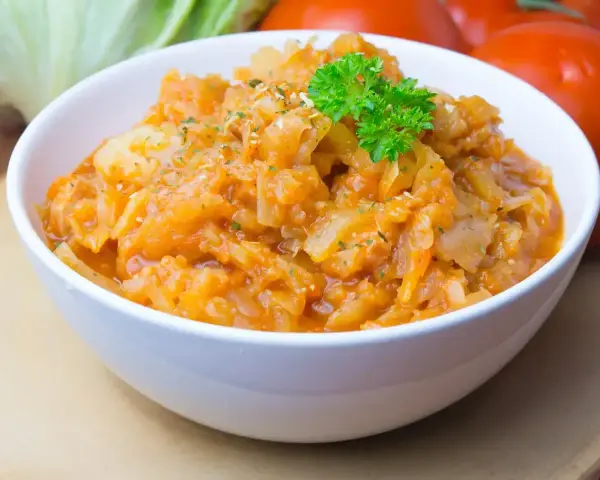 Pyszny bigos ze słodkiej kapusty, duszony z pomidorami i przyprawami, udekorowany natką pietruszki.