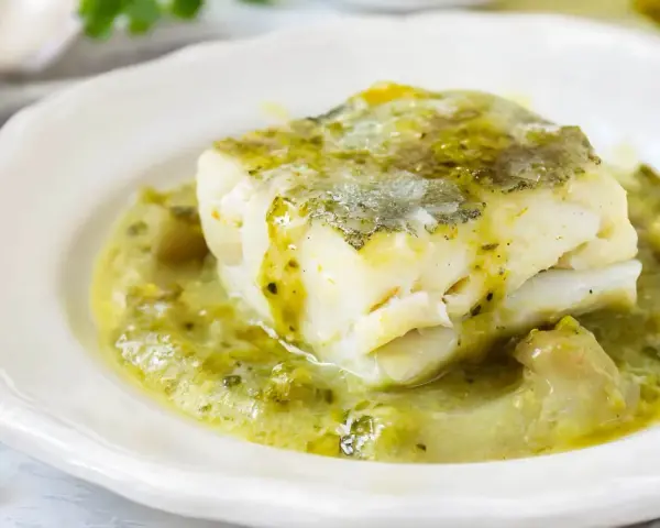 Un trozo de merluza a la vasca, jugoso y tierno, bañado en una salsa verde cremosa con trozos de pimiento.