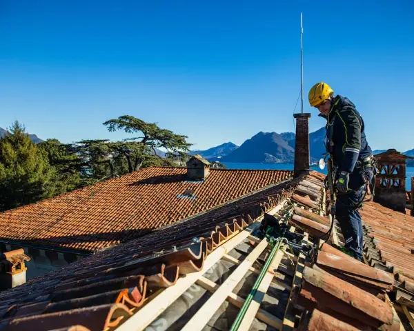 Operaio con imbracatura lavora alla costruzione tetti in legno, con vista su lago e montagne.