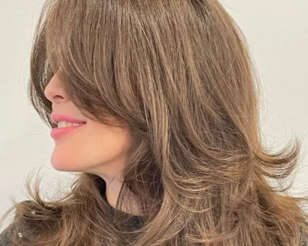 Mujer sonríe con un corte mariposa pelo largo, con capas que enmarcan su rostro.