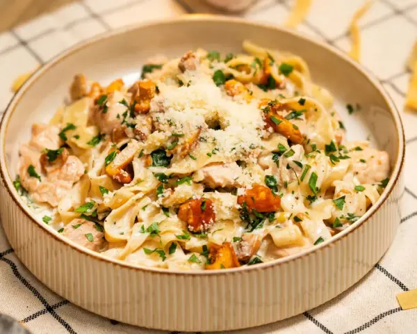 Pyszny makaron w sosie kurkowym z kawałkami kurczaka i posypany parmezanem.