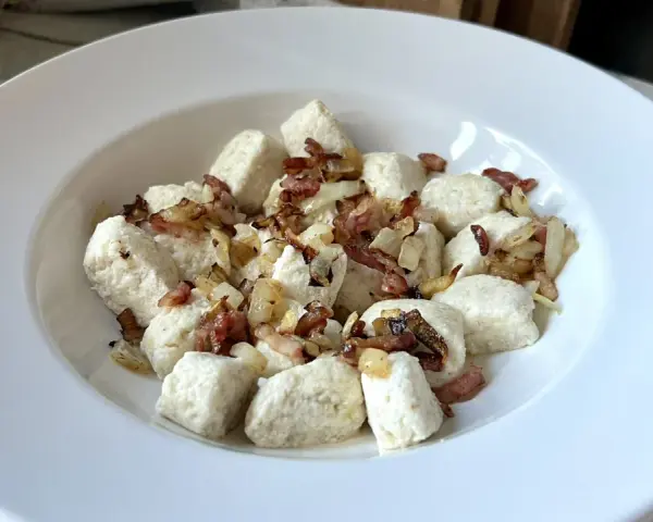 Pyszna keto kolacja z twarogiem w formie kluseczek, posypana chrupiącym boczkiem i cebulką.