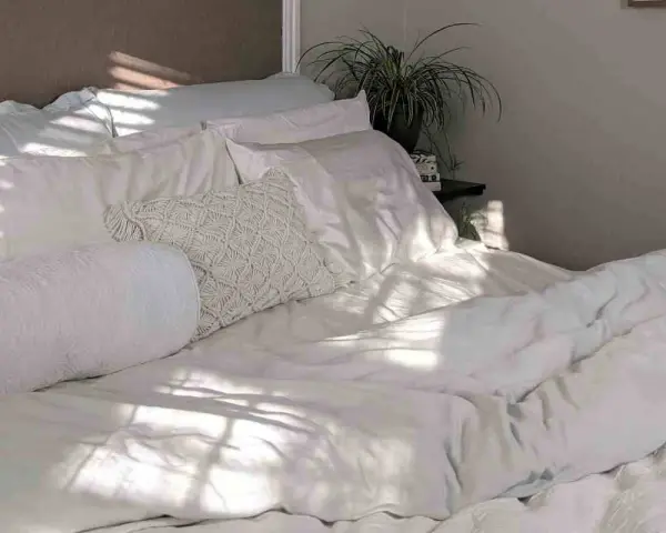 Cama blanca con luz solar filtrada. Aprende como lavar un edredón de plumas para mantenerlo esponjoso.