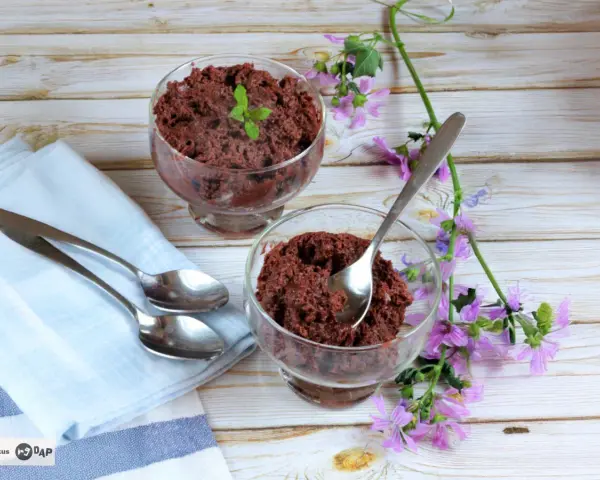 Dos copas de delicioso mousse de chocolate de la abuela, decoradas con menta y flores moradas, listas para disfrutar.