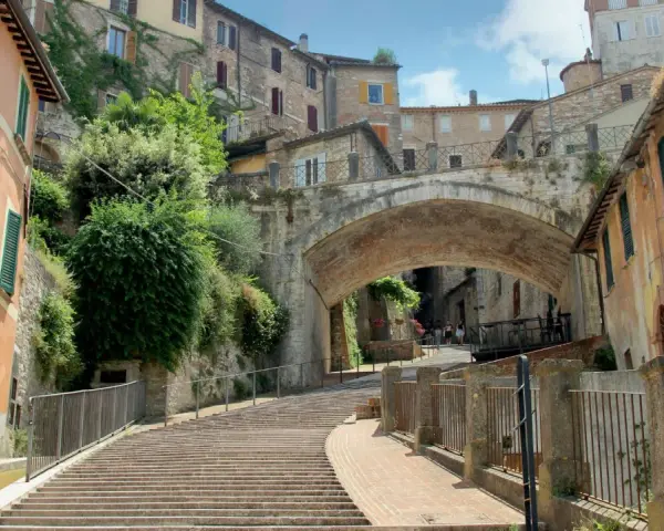 Perugia co zobaczyć: malownicze schody prowadzące pod zabytkowy most, otoczone kamiennymi domami i zielenią.