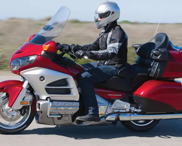 Mężczyzna w kasku jedzie lśniącym, czerwonym motocyklem turystycznym Honda Gold Wing.