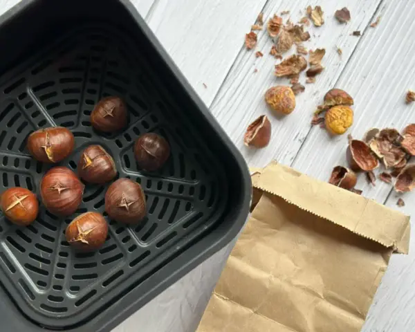 Châtaignes grillées dans le panier de l'air fryer, prêtes à être dégustées. Les écorces vides jonchent la table.