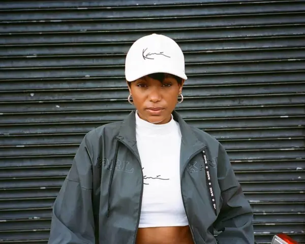 Kobieta w białej czapce z logo Karl Kani i kurtce tej marki. To kultowa marka streetwearowa.