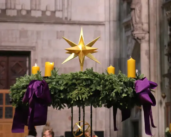 Ein Adventskranz mit vier gelben Kerzen und einem goldenen Stern, geschmückt mit lila Bändern. Seine Bedeutung liegt im Warten und Hoffen auf Weihnachten.