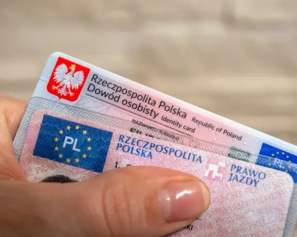 Dłoń trzyma polski dowód osobisty i prawo jazdy. To dokumenty, które pozwalają na swobodne podróżowanie, a prawo jazdy bezterminowe daje spokój na lata.