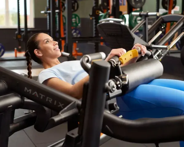 Femme souriante effectuant un hip thrust sur une machine de musculation, concentrée sur son entraînement.