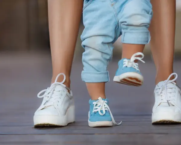 Małe niebieskie buciki na nogach dziecka, idealne na rozmiar buta 3 latka, obok białych sneakersów dorosłego.