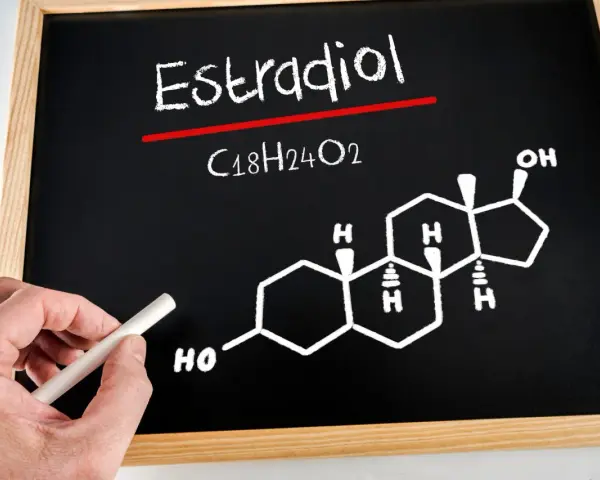 Estradiol co to za badanie? Na tablicy wzór chemiczny estradiolu (C18H24O2) i jego struktura. Ręka z kredą.