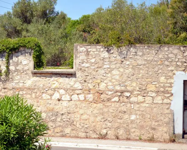 Un mur en pierre extérieur, avec des pierres irrégulières et du mortier, attend de restaurer son charme ancien. La végétation s'y accroche.