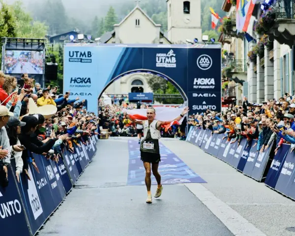 Biegacz z polską flagą przekracza metę UTMB Mont-Blanc. Tłum kibiców świętuje jego sukces.