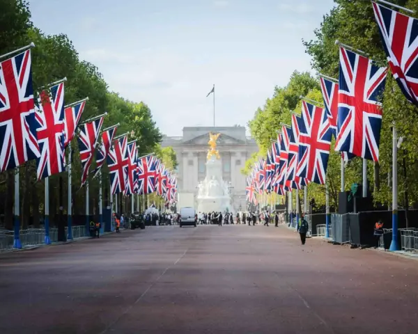 Allée bordée de drapeaux britanniques menant à un palais, avec des arbres et des gardes.