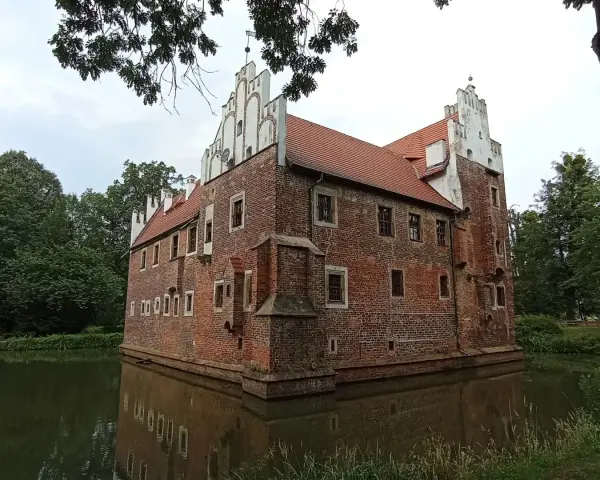 Zamek na wodzie w Wojnowicach, otoczony fosą, prezentuje ceglaną architekturę z białymi zdobieniami.