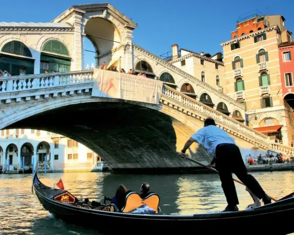 Gondola sotto il Ponte di Rialto, un'icona delle piazze Venezia, con edifici colorati e turisti che ammirano il panorama.