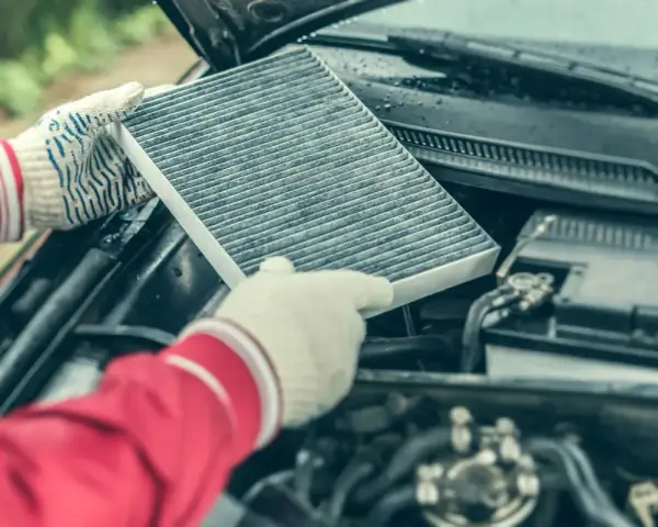 Hands in gloves hold a dirty cabin air filter, ready for replacement. This contrasts with the engine air filter, unseen but vital for car performance.