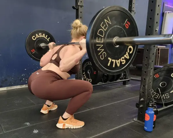 Kvinna utför en djup knäböj med skivstång. En del av hennes "russian squat routine" i gymmet.