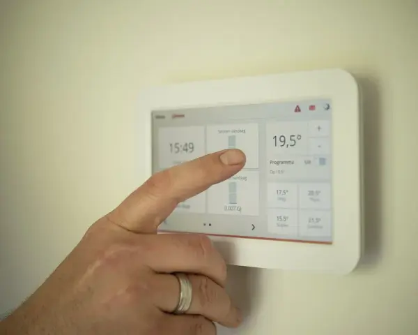 Dłoń dotyka ekranu termostatu, ustawiając temperaturę na 19,5°C. Idealne rozwiązanie na nadchodzący sezon grzewczy.