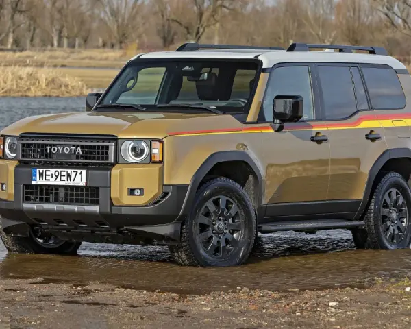 Złoty Toyota Land Cruiser Prado z kolorowymi pasami na boku, wjeżdża do wody.