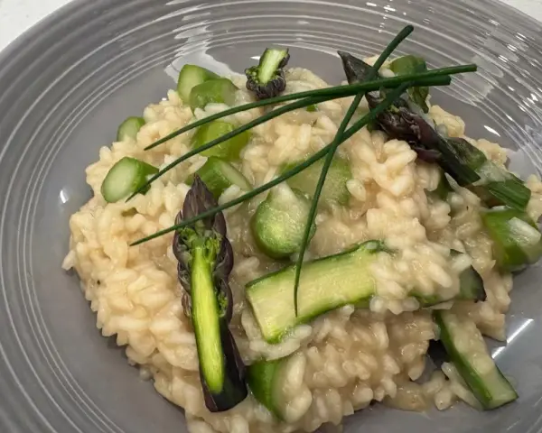 Kremowe risotto z zielonymi szparagami i szczypiorkiem na szarym talerzu.