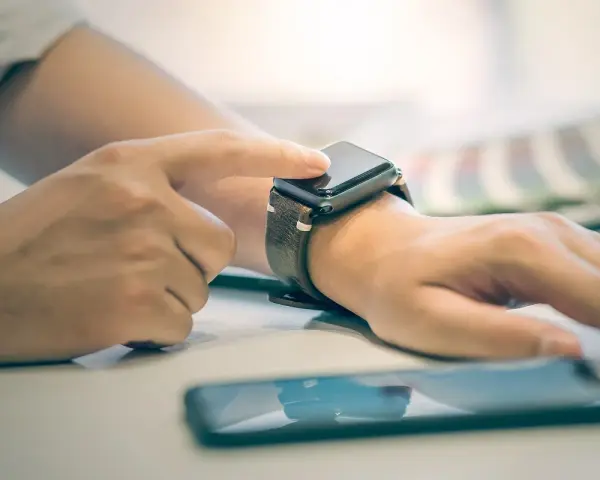 Dłoń z zegarkiem na nadgarstku, palec dotyka ekranu, pokazując jak włączyć bluetooth w smartwatch.