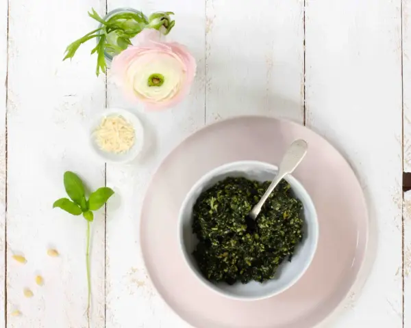 Schüssel mit frischem Basilikum-Pesto, Pinienkernen, Parmesan und einer zarten rosa Blume. Ein Hauch des originalrezepts.