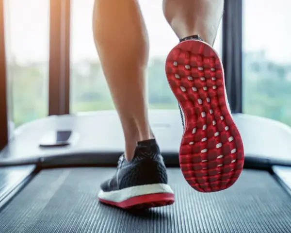 Gambe che corrono su un tapis roulant, con una scarpa rossa e nera in primo piano. Un'ottima immagine per chi vuole capire come iniziare a camminare.