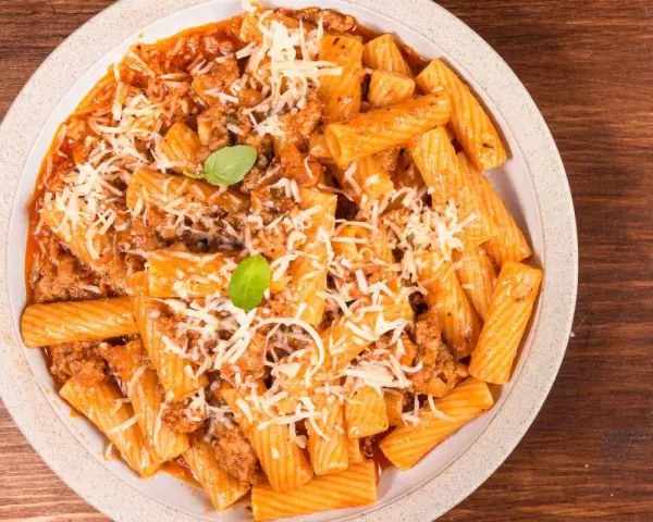 Un piatto invitante di pasta alla zozzona, con rigatoni conditi con un ricco ragù e abbondante parmigiano grattugiato, guarnito con basilico fresco.