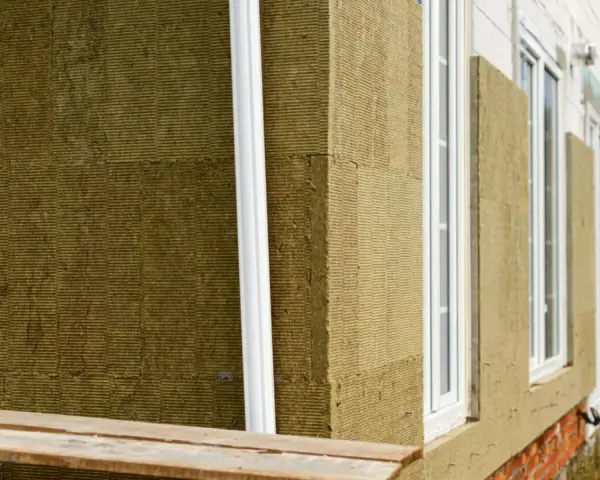 Detalle constructivo SATE: aislamiento de lana mineral en fachada, con ventanas blancas y tubería de desagüe.