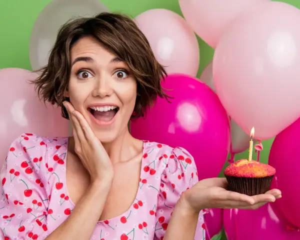 Uśmiechnięta dziewczyna z babeczką i świeczką, otoczona balonami. Idealne życzenia na 19 urodziny!