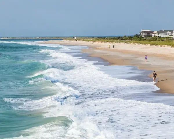Waves crash on the shore at Wrightsville Beach, where people enjoy a run and a stroll, showcasing some of the relaxing things to do.