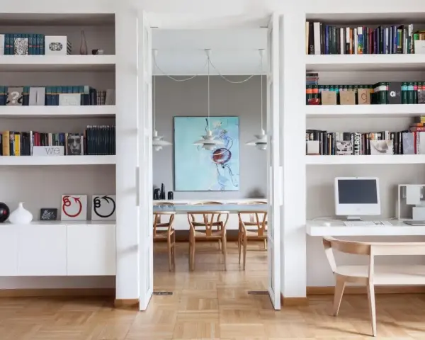 Ampia libreria in cartongesso con libri, computer e decorazioni. Si intravede una sala da pranzo con un quadro astratto.