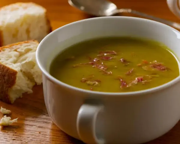 Un bol de soupe de pois cassés fumante, garnie de lardons, avec du pain croustillant à côté. Un délice réconfortant.