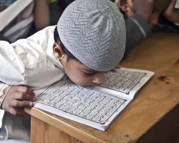 Chłopiec w czapce na głowie pochyla się nad Kor'anem, ucząc się o senegalskiej religii.