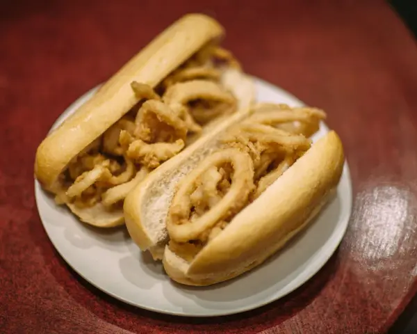 Dos bocadillos de calamares fritos en pan blanco sobre un plato blanco.