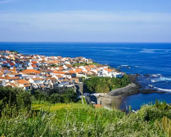 Malownicze miasteczko na wybrzeżu Portugalii, z białymi domami i pomarańczowymi dachami, nad błękitnym oceanem. Ceny wakacji w Portugalii mogą być zaskakująco przystępne.