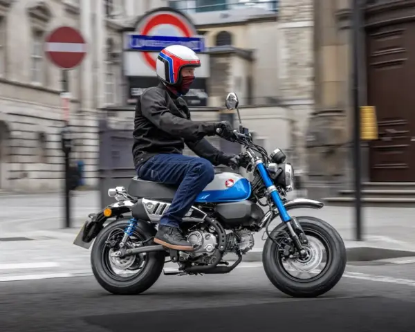 Mężczyzna w kasku jedzie na małym motocyklu, przypominającym boda boda, po ulicy miasta.