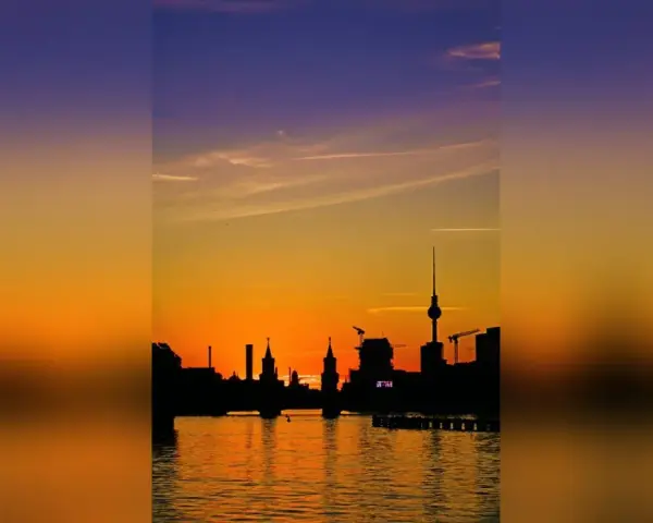 Silhouetten der Berliner Skyline spiegeln sich im Wasser. Ein dramatischer Sonnenuntergang taucht den Himmel in Orange- und Violetttöne.