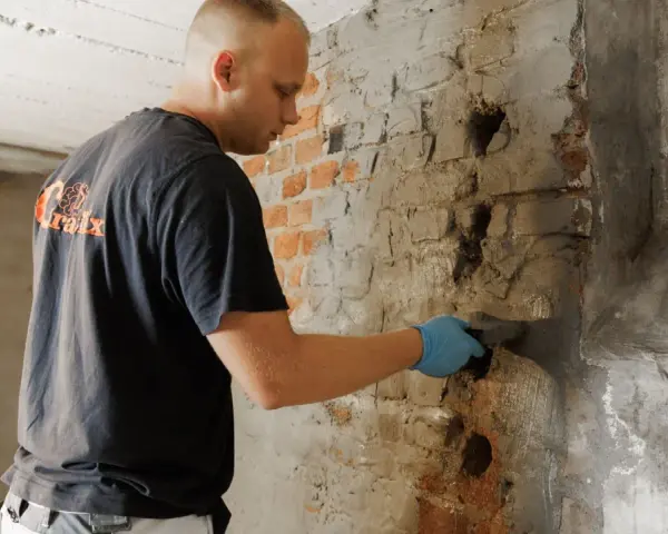 Mann verputzt feuchten Kellerwand.