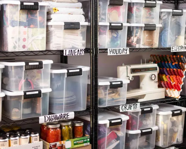 Organized basement storage ideas with labeled clear bins for linens, holiday items, crafts, electronics, and dishware.