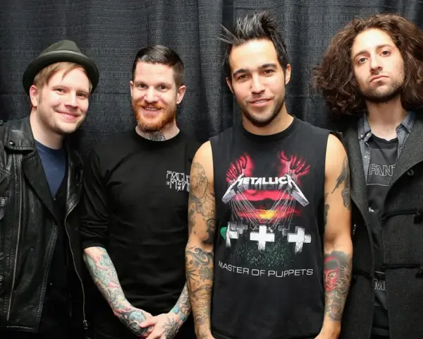 Czterech mężczyzn z zespołu Fall Out Boy pozuje do zdjęcia na tle czarnej kurtyny.