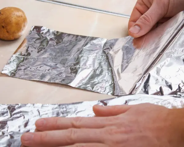 Ręce rozwijają folię aluminiową obok ziemniaków. Zastanawiasz się, gdzie wyrzucić folię aluminiową?