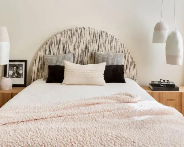 Camera da letto con testiera a semicerchio, cuscini decorativi e coperta rosa. Lampade a sospensione e comodini in legno completano l'arredamento, creando camere aesthetic.