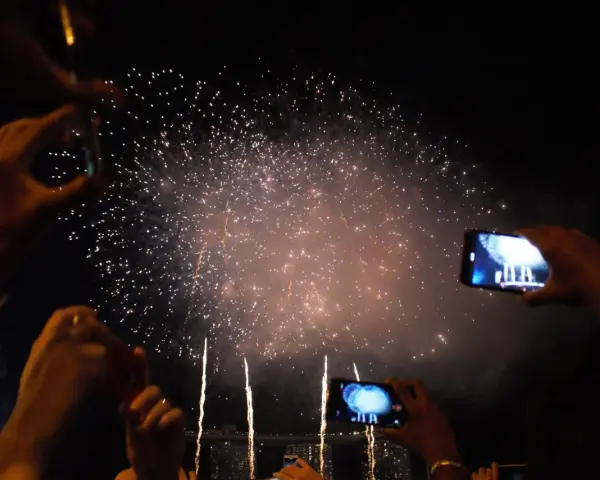 Des mains filment un magnifique feu d'artifice dans le ciel nocturne, capturant la magie de l'instant.