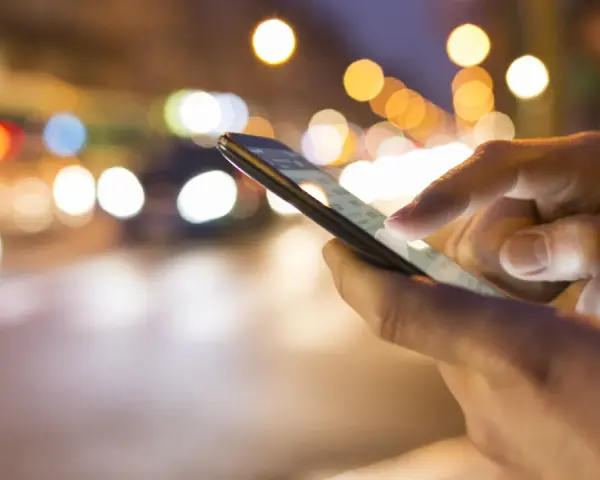 Hände bedienen ein Smartphone im nächtlichen Stadtverkehr. Tipps, um das iPhone schneller machen, sind hier vielleicht gesucht.
