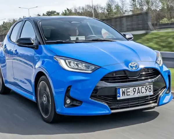 Błękitna, nowa Toyota Yaris z czarnym dachem pędzi po drodze.