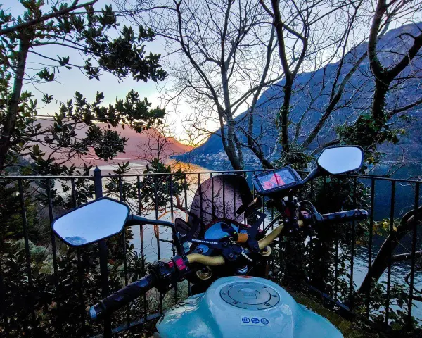 Manubrio moto con vista panoramica sul Lago di Como al tramonto. Un invito a esplorare i punti panoramici in moto.